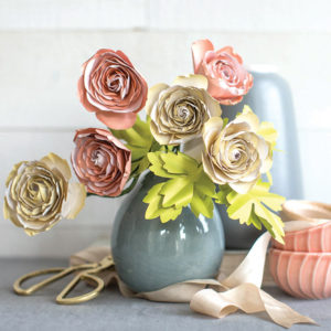 six frosted paper ranunculus flowers with leaves in vase