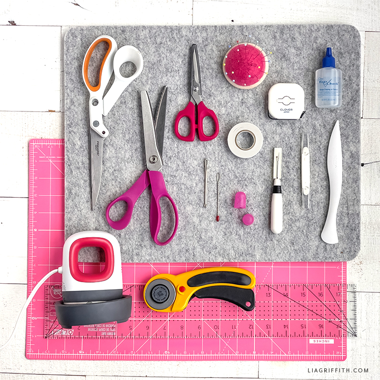 An assortment of crafting tools laying on a gray felt mat and a pink cutting board.