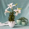 Easter lily crepe paper flower sits in pot in front of blue cloth background with two potted crepe paper plants behind it
