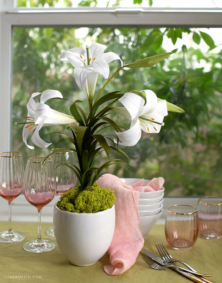 Easter lily crepe paper flower sits in pot by windowsill amidst table setting