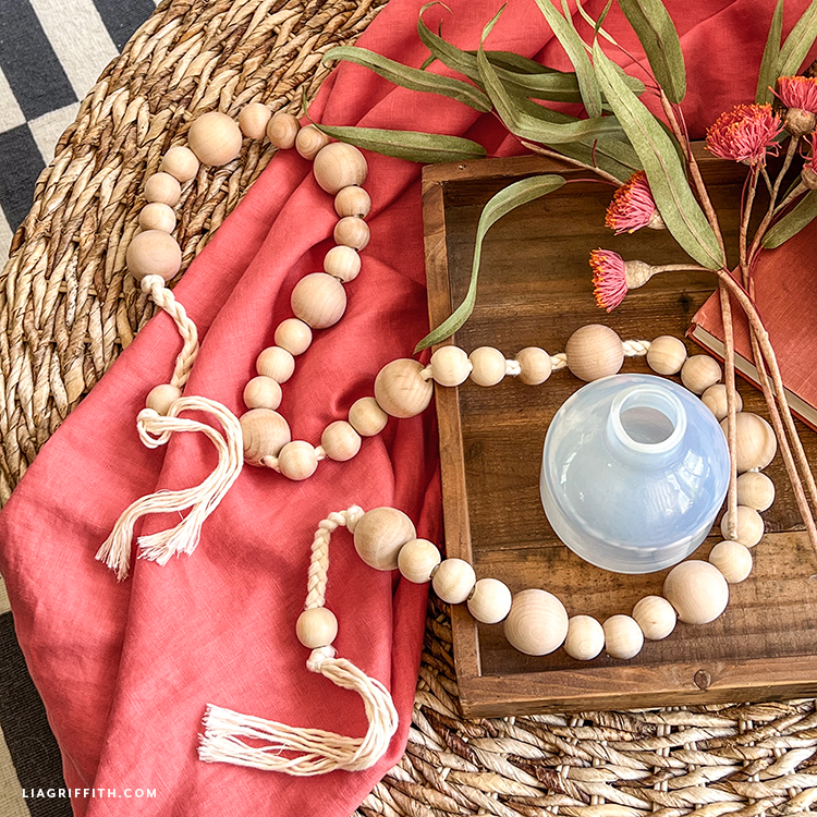 A long string of wooden beads sitting on a wooden mat and wooden tray with plants and jars.